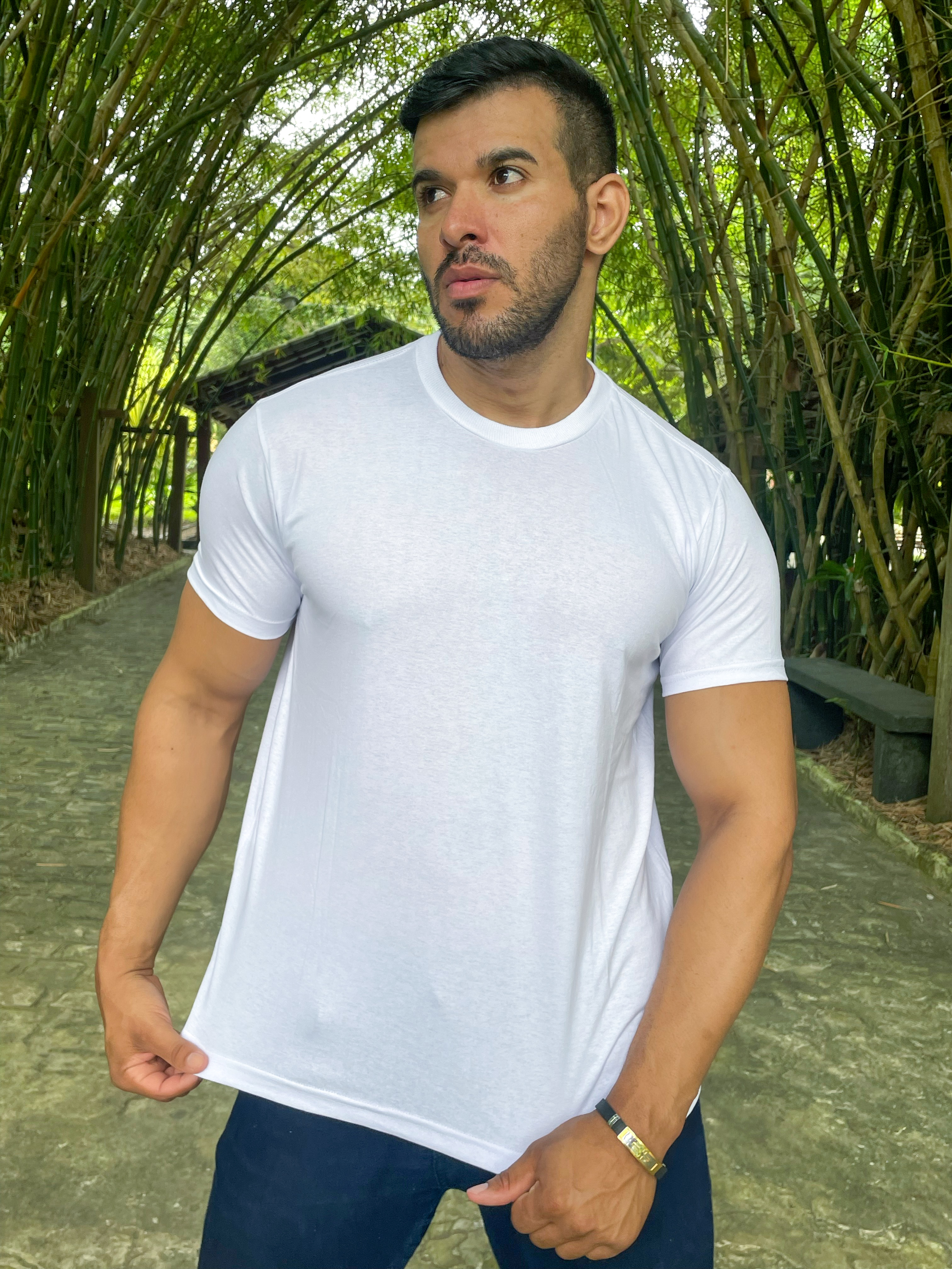 Homem posando em ambiente natural com camiseta branca, rodeado por bambus.